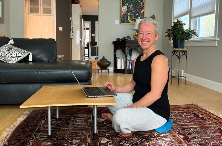 Smiling woman sitting on the floor, working on a laptop.